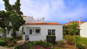A white building with a red-tiled roof, a paved pathway, and a garden with pink flowers. - Casa Scarlett, Walk to beach, Communal Pool (Carvoeiro)