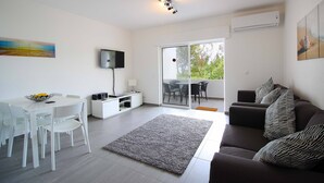 A modern living room with a dining area, a sofa, a flat-screen TV, and a large window. - Casa Scarlett, Walk to beach, Communal Pool (Carvoeiro)