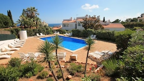 A swimming pool with lounge chairs, surrounded by greenery and buildings. - Casa Scarlett, Walk to beach, Communal Pool (Carvoeiro)