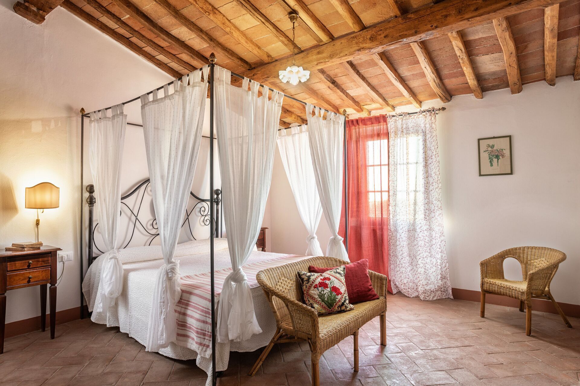 Une chambre à coucher avec un lit à baldaquin, une chaise en osier, une table de chevet et un rideau rouge.