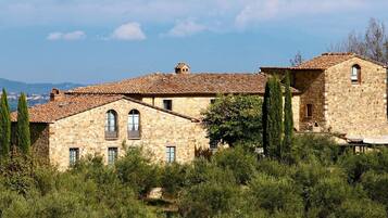 Un bâtiment en pierre, doté d’un toit en tuiles, entouré de verdure et offrant une vue sur le paysage urbain lointain.