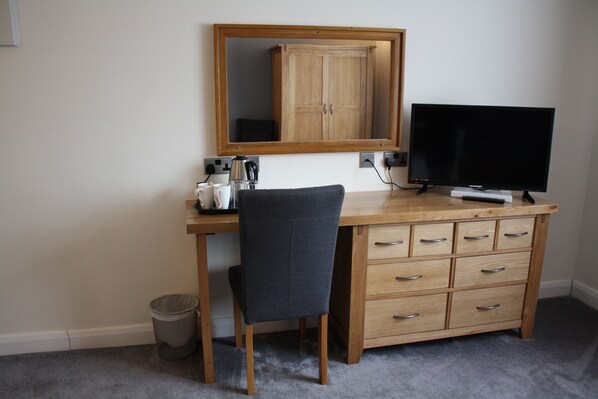 A wooden desk with a chair, a television, a mirror, and a cabinet.