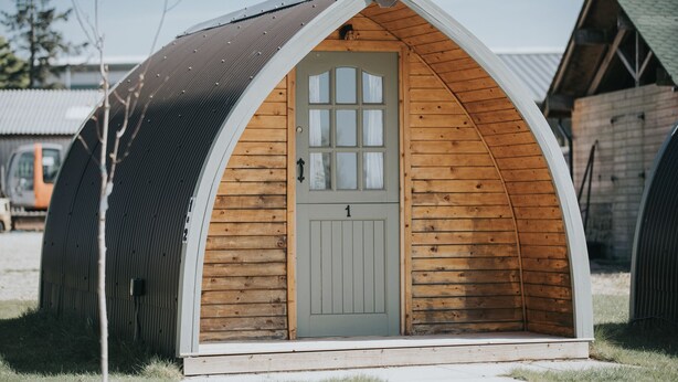 Una pequeña estructura de madera, parcialmente abierta, con una puerta y ventanas, rodeada de construcciones similares.