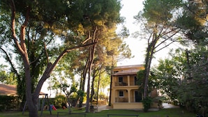 A two-story building with a balcony, surrounded by trees and a playground. - Zarkadis Beach Apartments (Zakynthos)