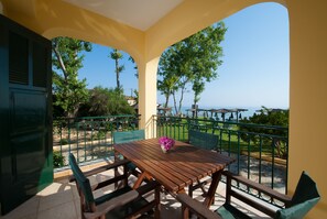 A wooden table with chairs and a vase of flowers on a balcony with a view of the sea.