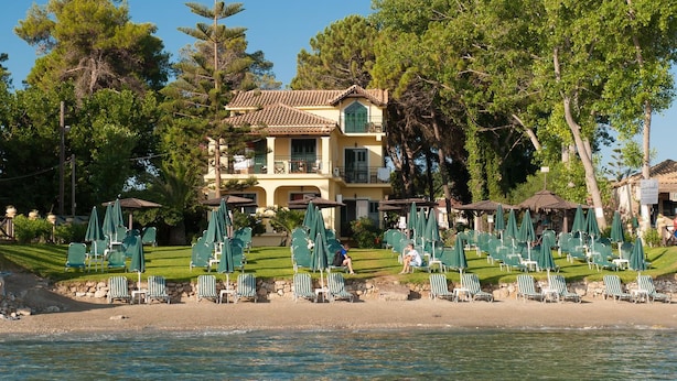 A beachfront property with a large building, multiple green umbrellas, and lounge chairs arranged on the sand. - Zarkadis Beach Apartments (Zakynthos)