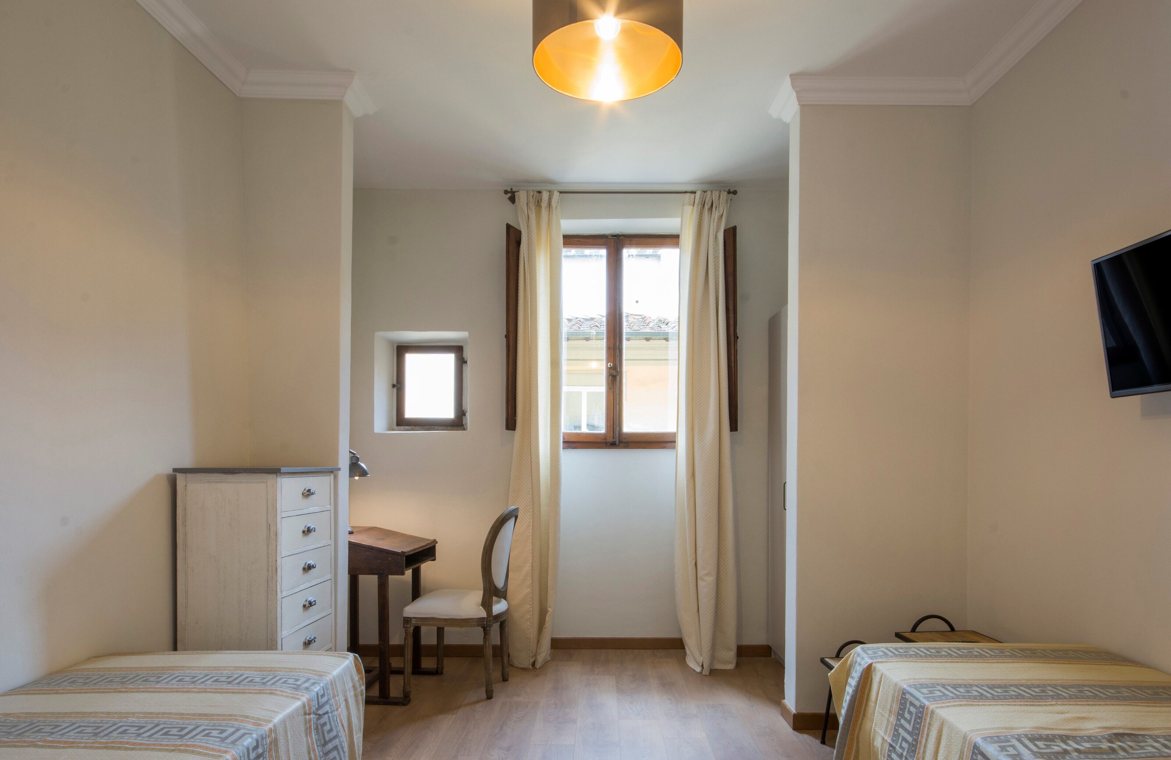 A bedroom with two beds, a desk, a chair, a dresser, and a window with curtains.