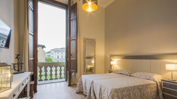 Quarto de hotel com uma cama grande, mesas de cabeceira, um espelho e vista da cidade através de uma porta aberta.