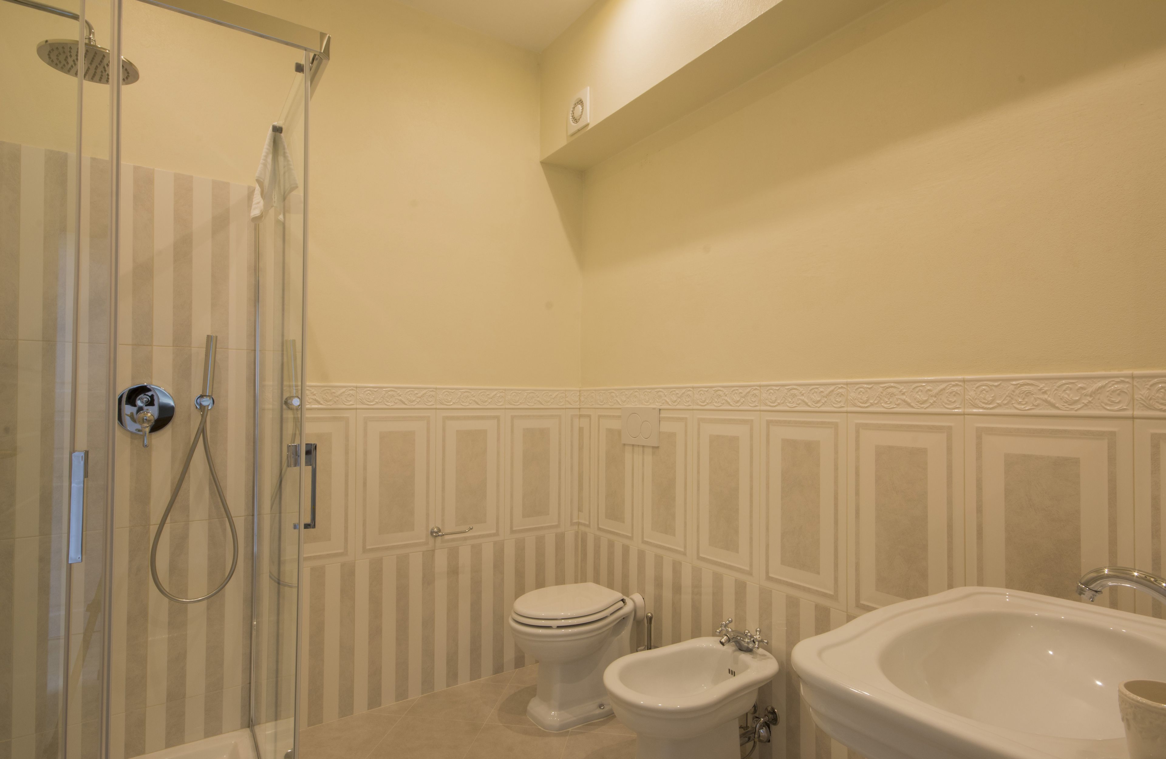 Een badkamer met een douchecabine van glas, een toilet, een bidet en een wastafel.
