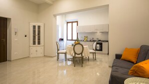 Uma sala de estar moderna com área de jantar, cozinha ao fundo e porta que dá para outro cômodo.