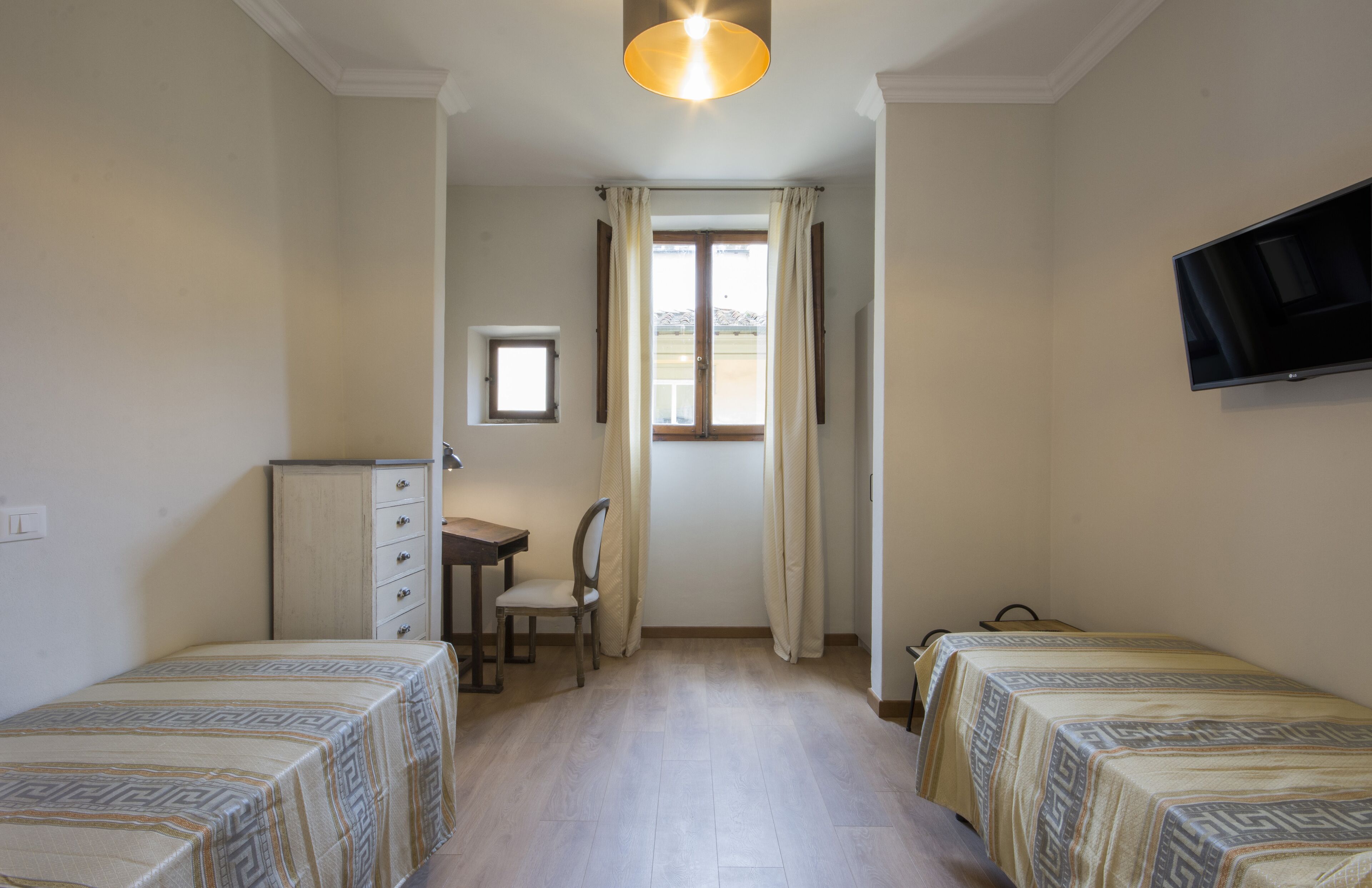 Una habitación con dos camas, un escritorio, una silla, un televisor y una ventana con cortinas.
