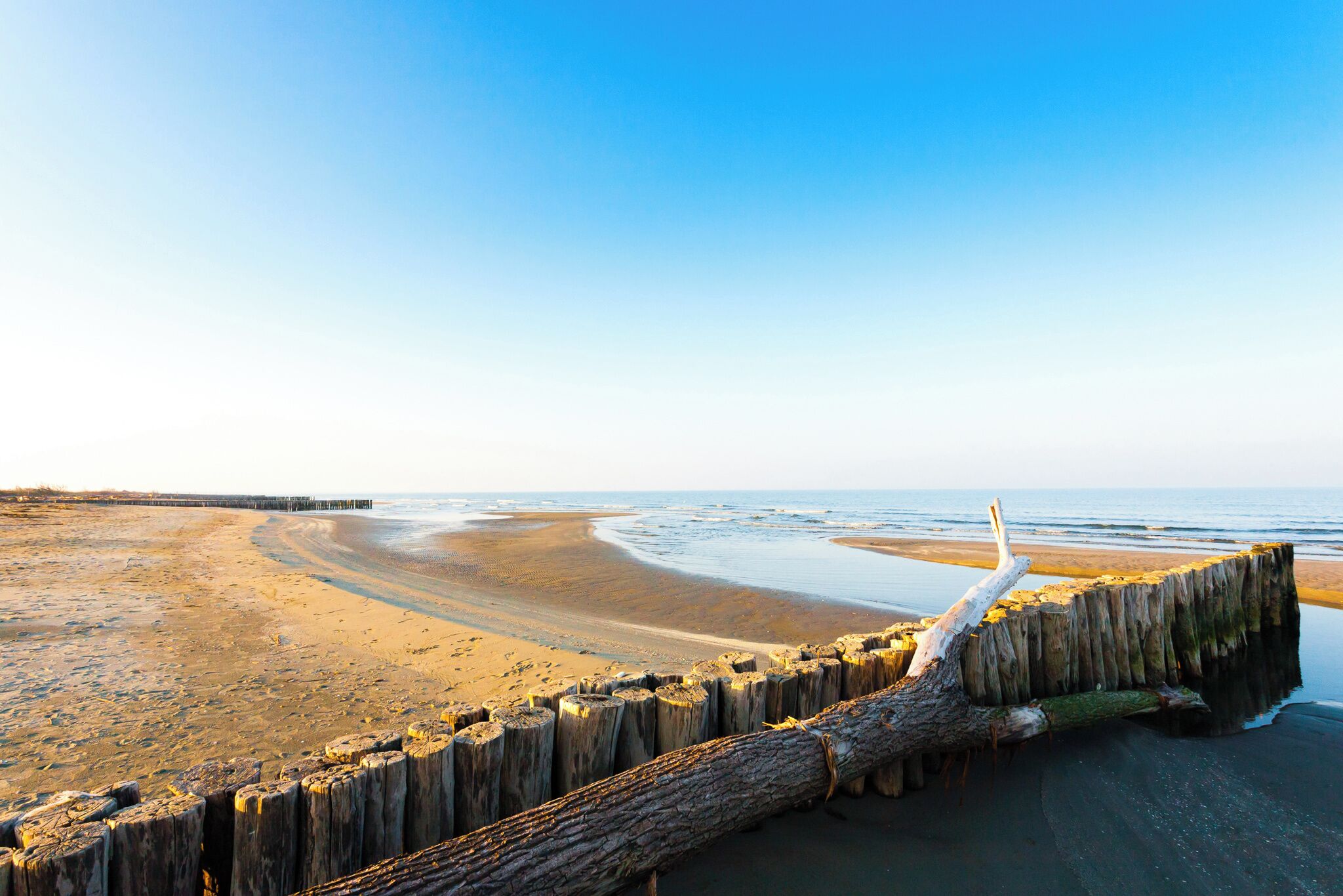 Ein Strand mit einem hölzernen Wellenbrecher und einer Mole, die ins Wasser führt.