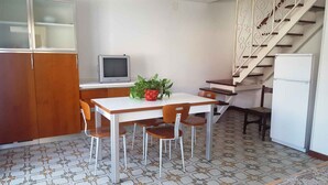 Een kleine keuken met een eettafel, stoelen, een televisie en een koelkast.