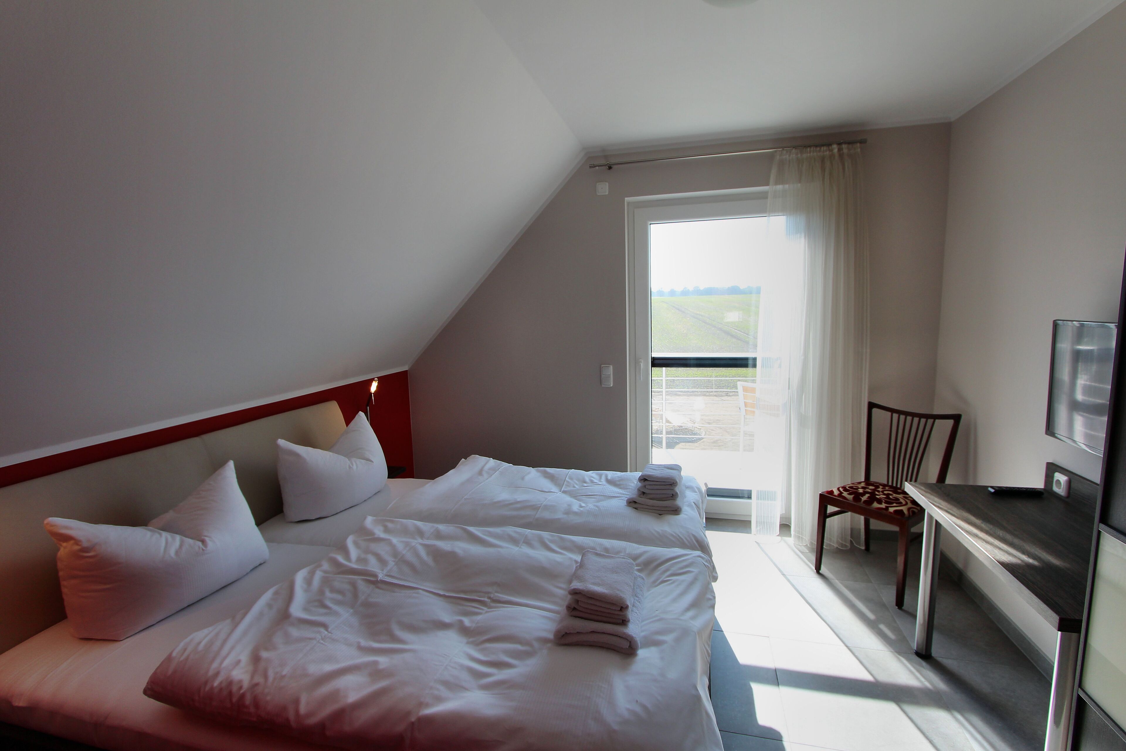 A hotel room with two beds, a desk, and a chair. There is a large window with curtains, and a TV on the wall.