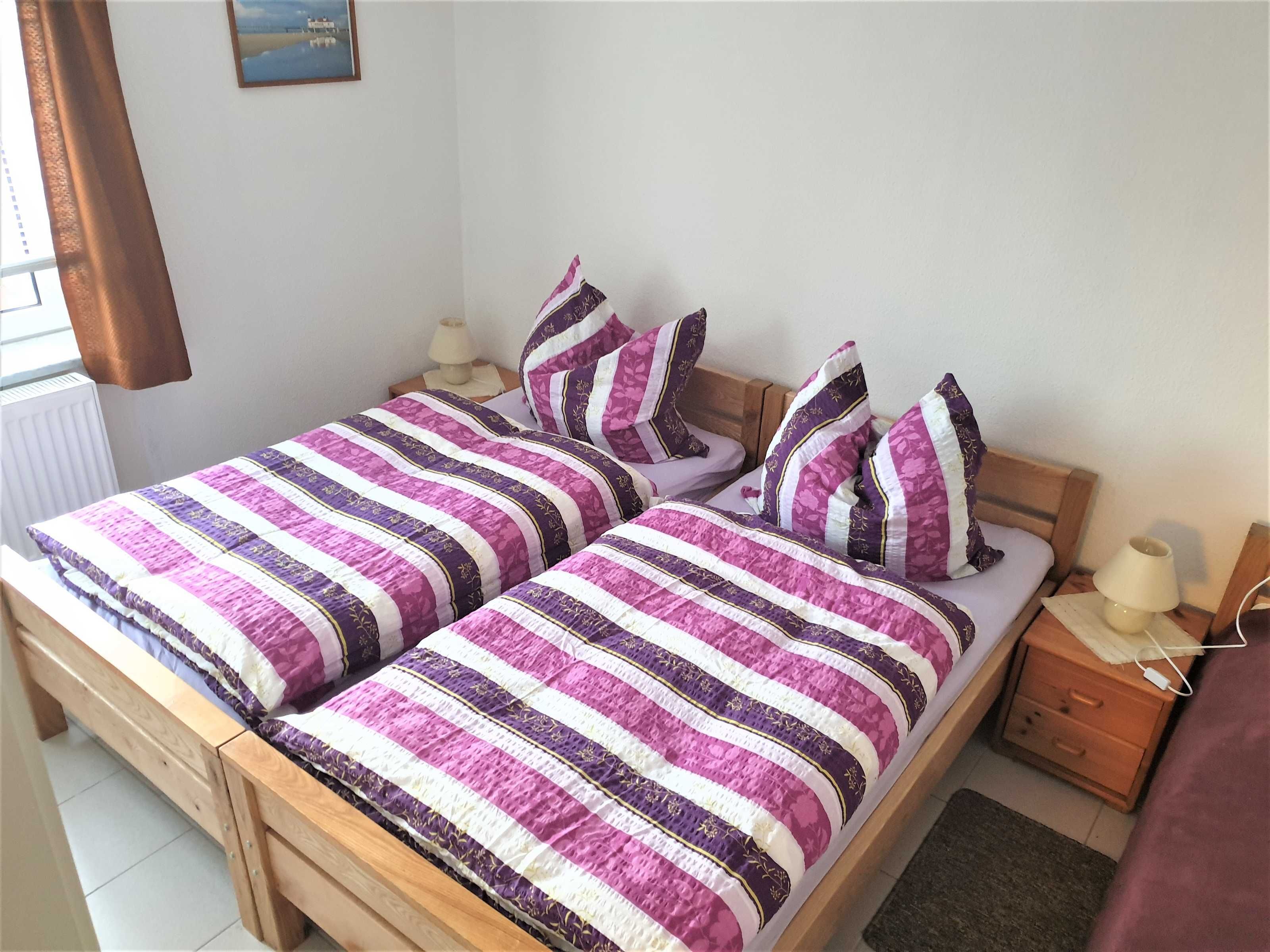 A double bed with a striped bedspread, two bedside tables with lamps, a wooden headboard, and a small nightstand with a lamp.