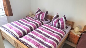 Ein Doppelbett mit gestreifter Bettdecke, zwei Nachttische mit Lampen, ein Holz-Kopfteil und ein kleiner Beistelltisch mit einer Lampe.