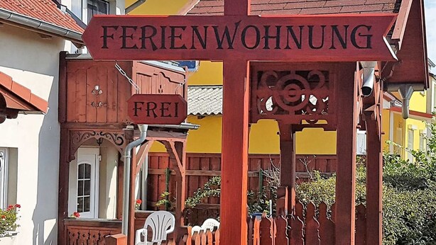 Ein Holzschild mit der Aufschrift 'FERIENWOHNUNG' und 'FREI', das eine Ferienwohnung oder ein Gästehaus kennzeichnet.
