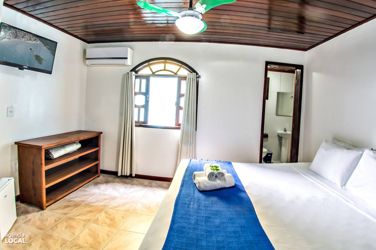 A hotel room with a bed, a wooden desk, a TV, and a window with curtains.