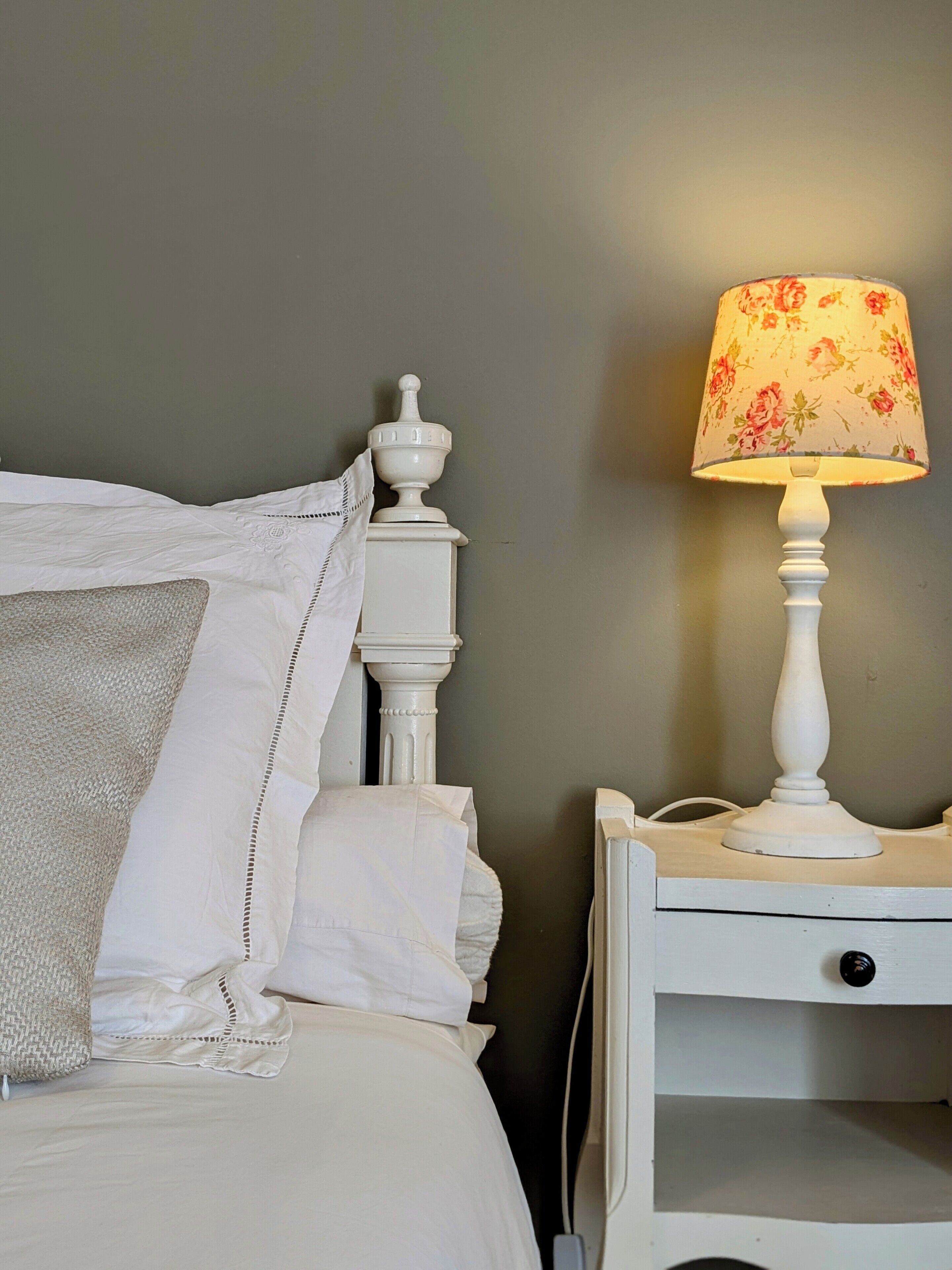 A neatly made bed with white linens and a white nightstand beside it.