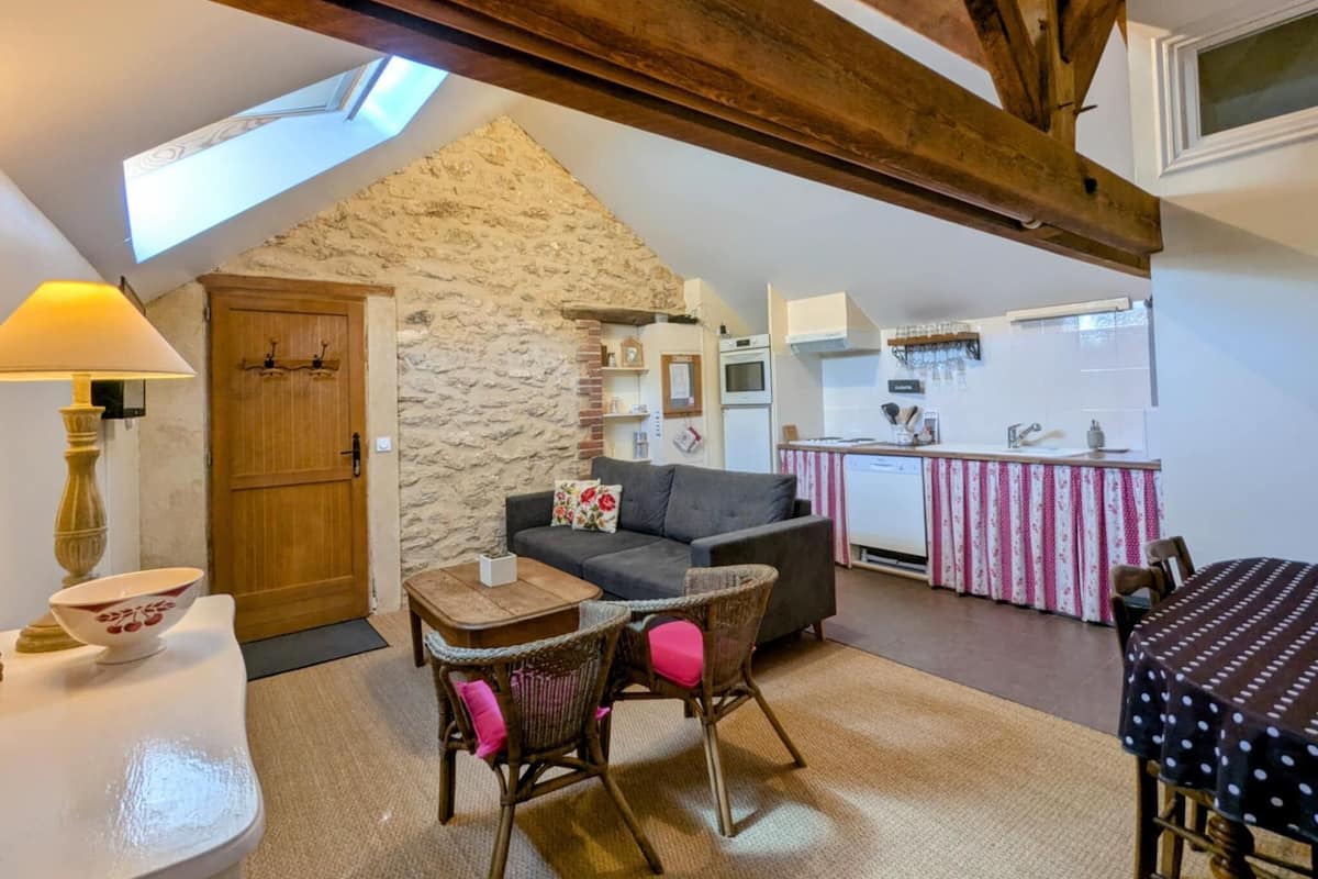 Un acogedor espacio tipo loft con pared de piedra, techo de madera, kitchenette y comedor con mobiliario de mimbre.