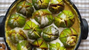 Un recipiente redondo para hornear con frutas verdes en rodajas y azúcar sobre un mantel a cuadros.