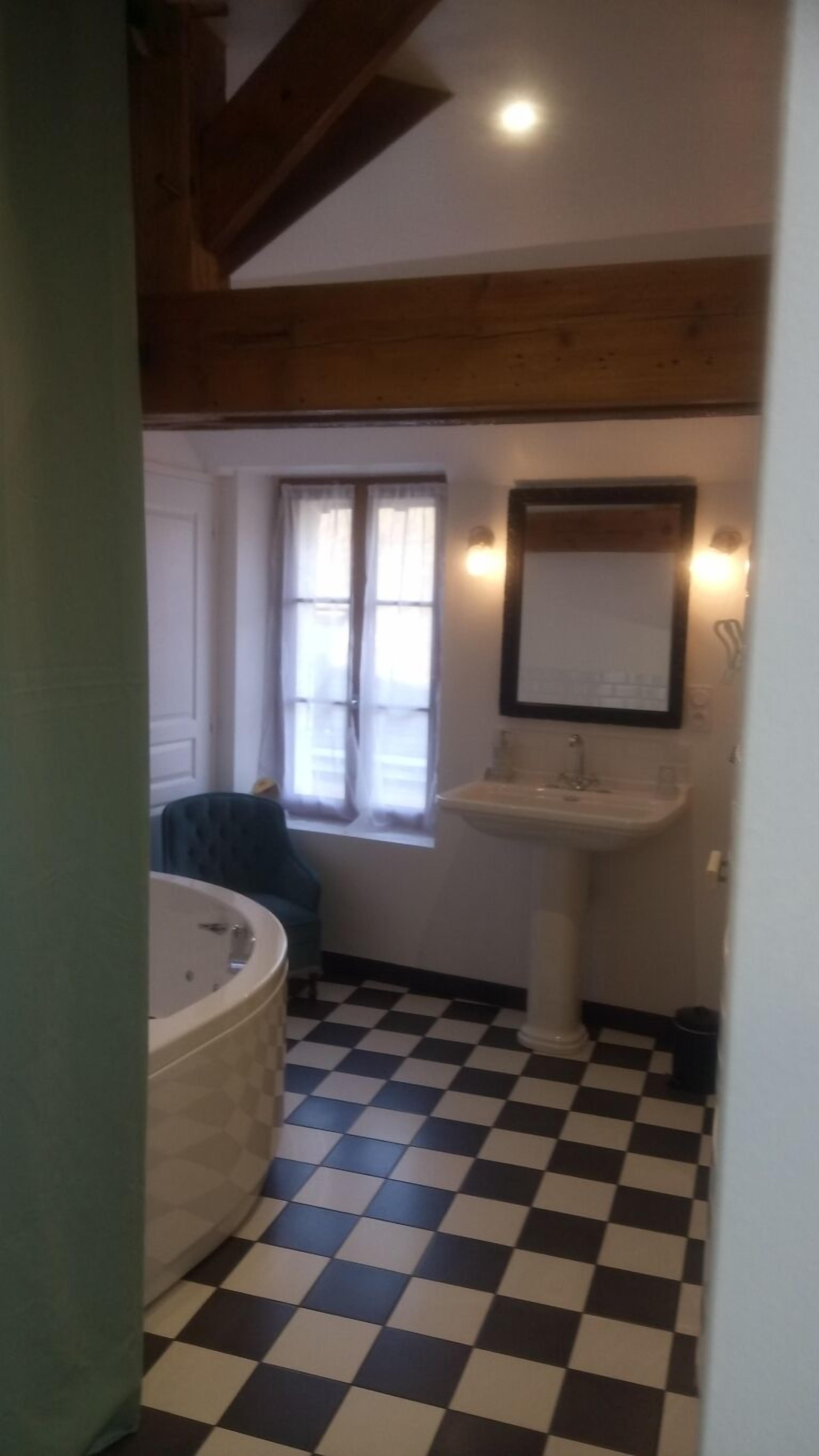 Une salle de bain avec un carrelage à motifs, une baignoire, un lavabo et une fenêtre avec des rideaux.