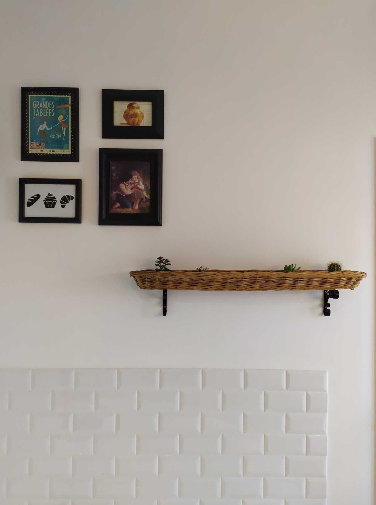 Una pared con cuatro cuadros enmarcados, un estante de mimbre con plantas y una chimenea con diseño de ladrillo blanco.