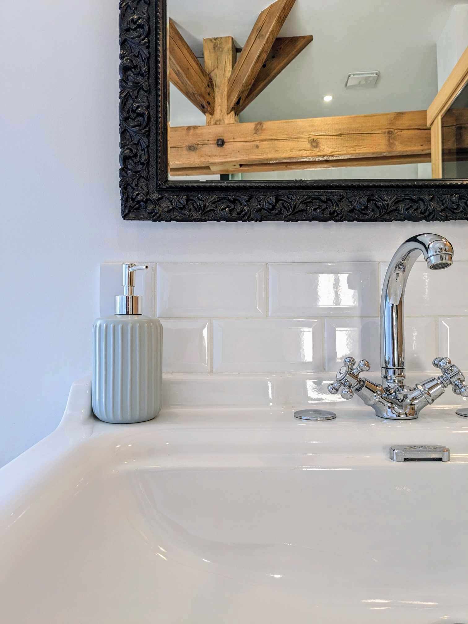 Une salle de bain avec un lavabo blanc, un robinet chromé et un miroir doté d’un cadre noir orné.
