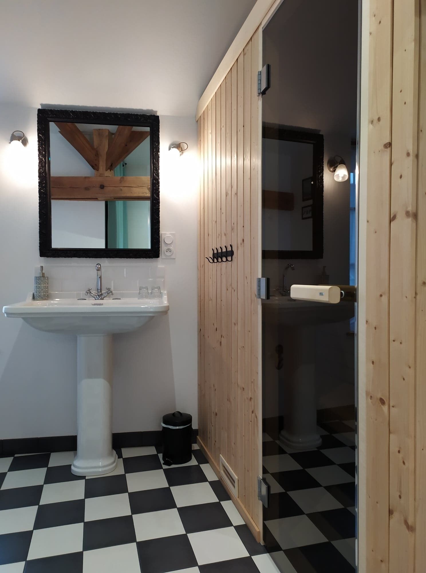 Ein Badezimmer mit einem weißen Standwaschbecken, einer Holz-Kommode und einem schwarz-weißen Schachbrettboden.