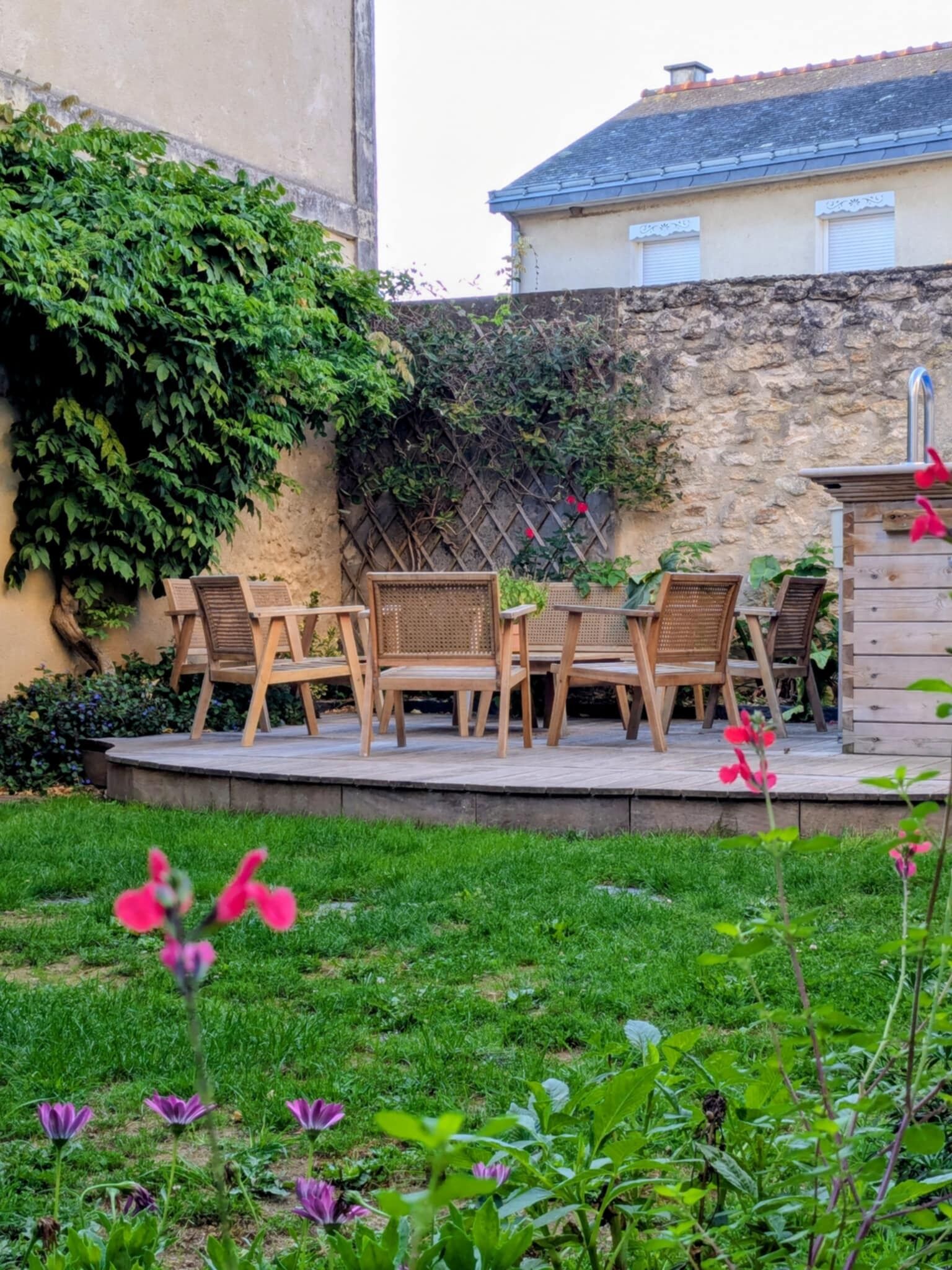 An outdoor patio with wooden furniture, a stone wall, and a garden with flowers.