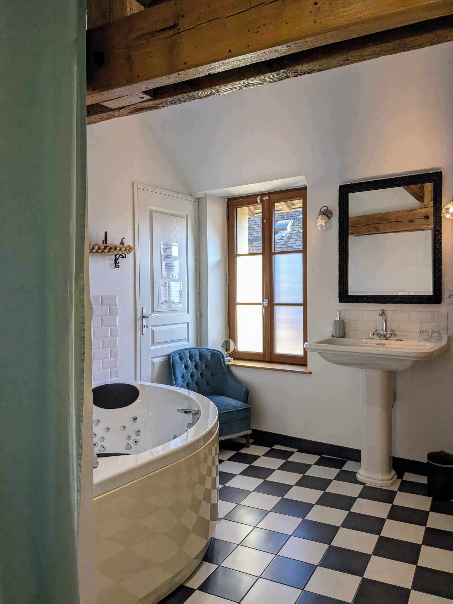 Ein Badezimmer mit Schachbrettboden, einer Badewanne, einem Waschbecken, einem Spiegel und einem Fenster mit Holzbalken.