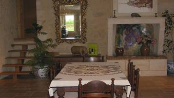 A dining area with a table set for six, surrounded by wooden chairs. A large mirror hangs above the table, and a fireplace with a colorful mural is visible in the background.