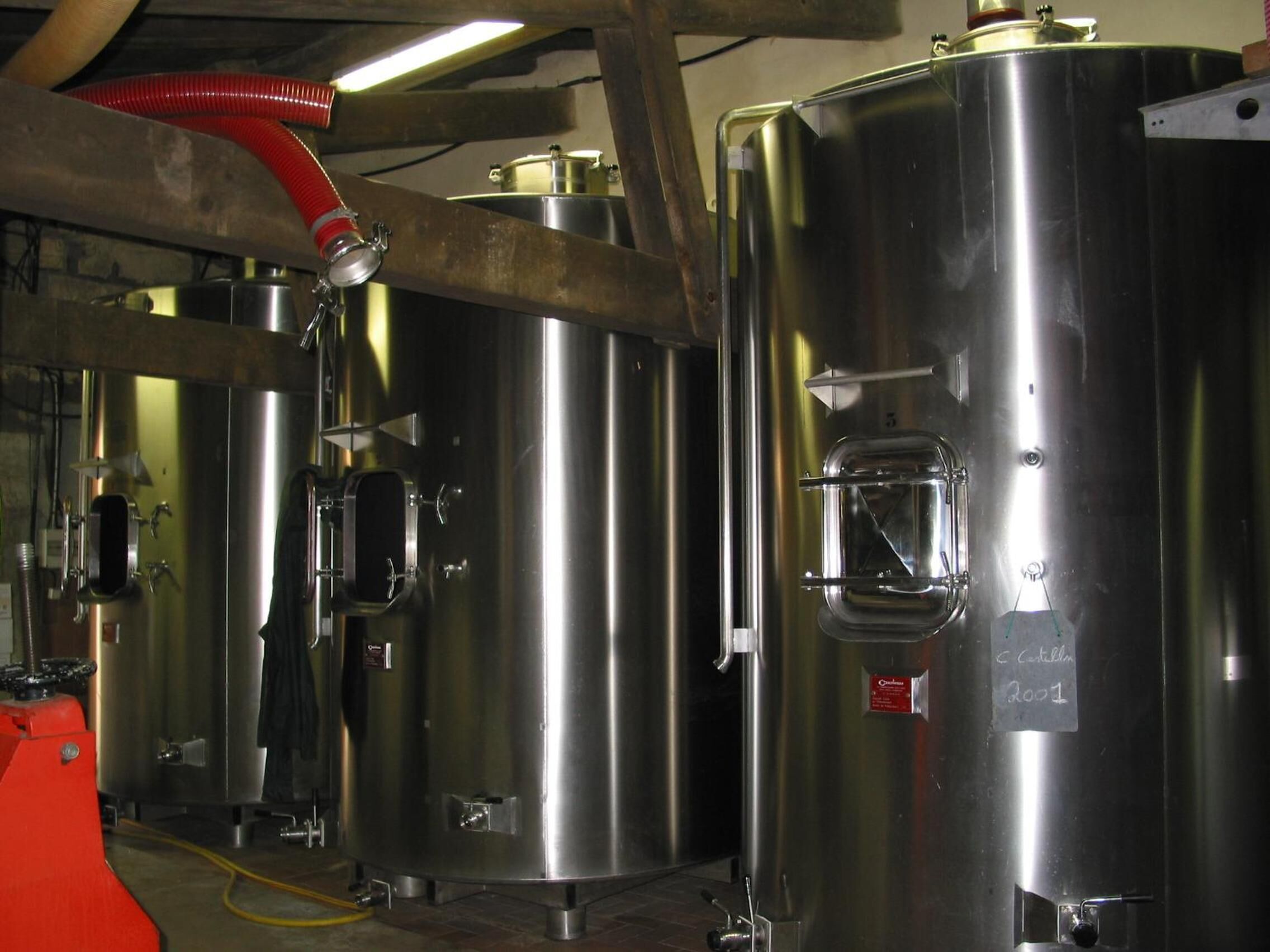 Stainless steel industrial tanks in a facility with visible piping and a wooden beam structure.