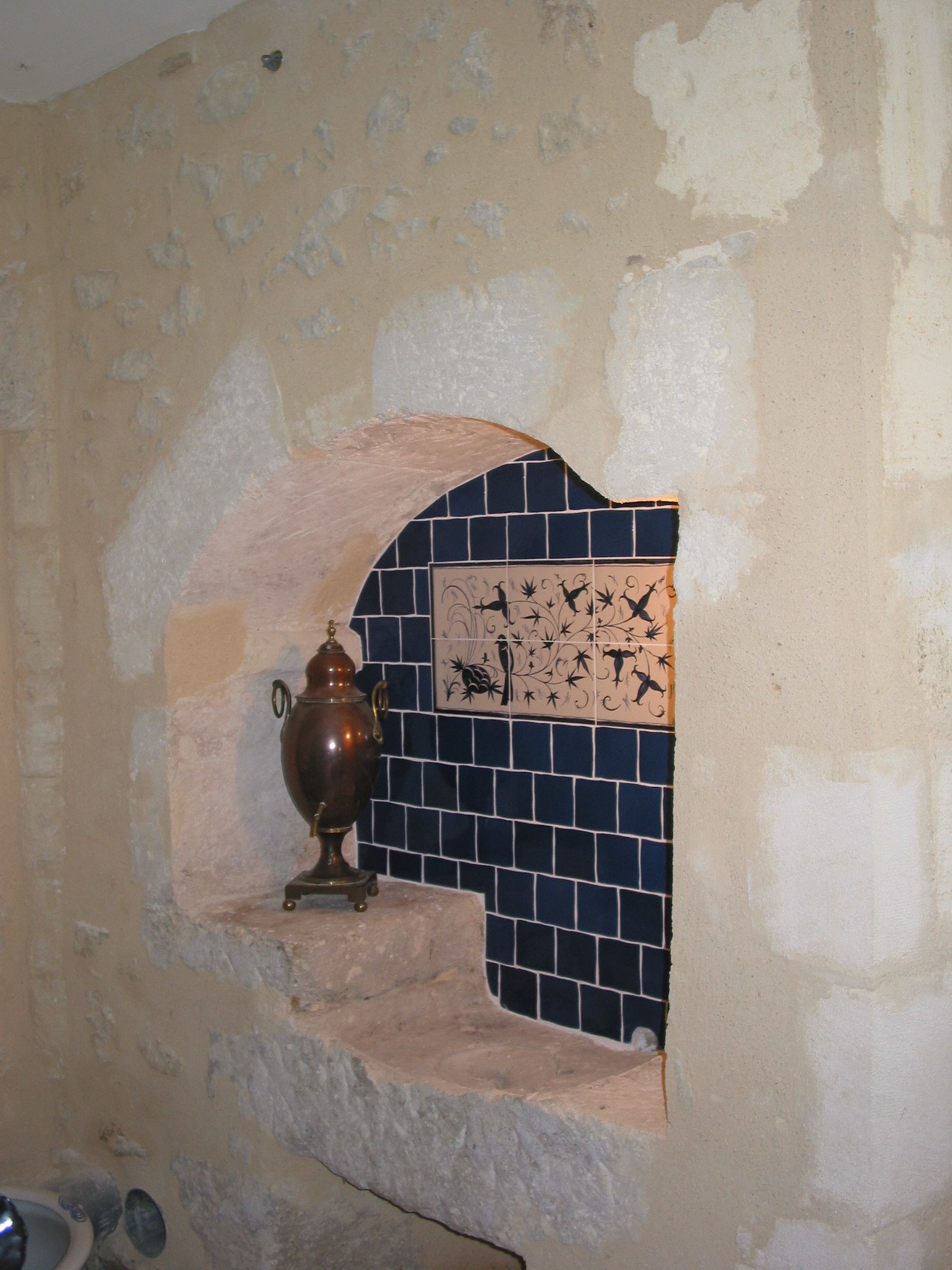 A stone wall with a tiled section featuring a bird and floral design.