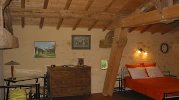 Ein rustikales Schlafzimmer mit freiliegenden Holzbalken, einem hölzernen Schminktisch und einem Bett mit orangefarbener Bettwäsche, sowie zwei Wandleuchten.