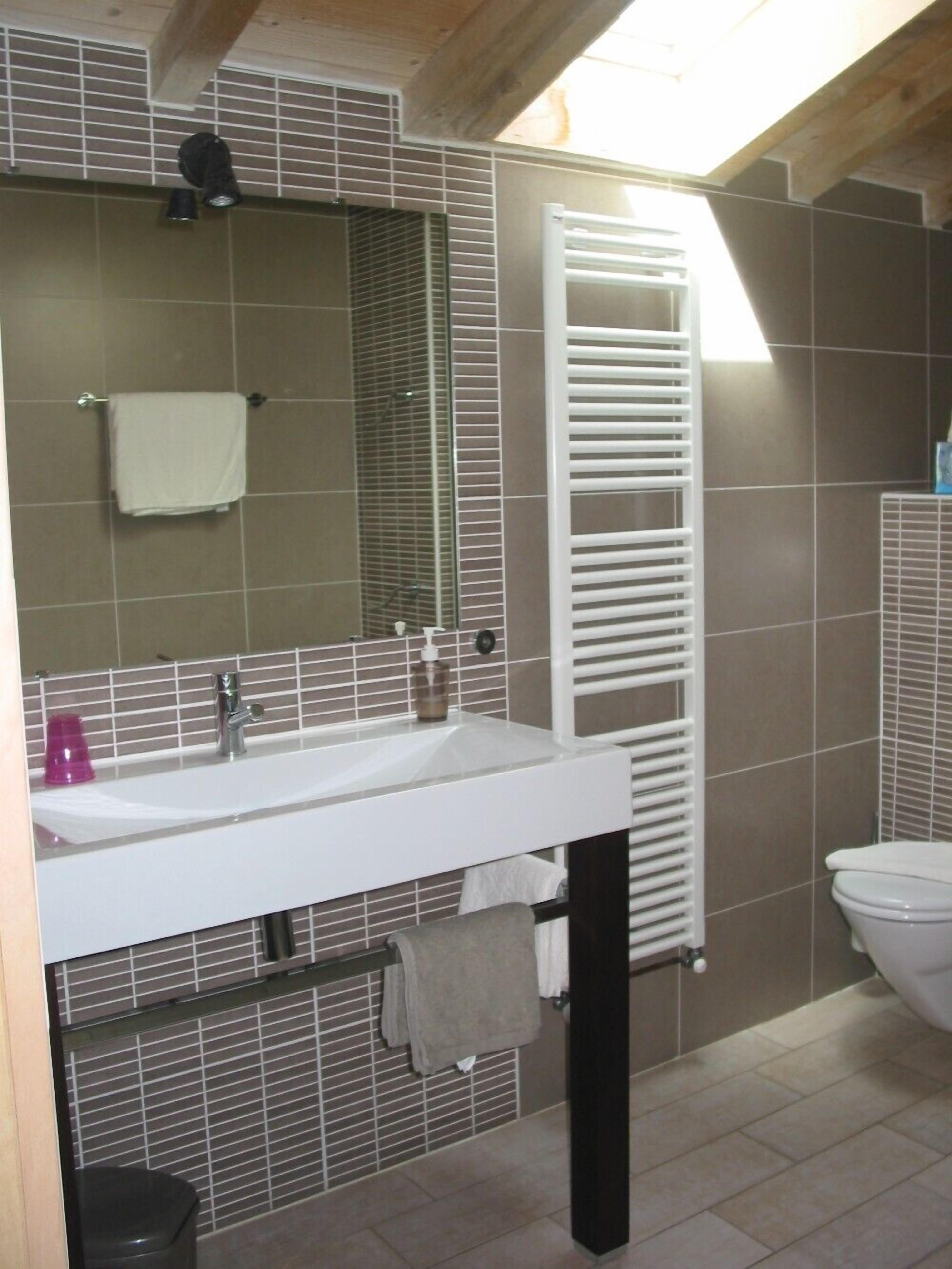 A bathroom with a white sink, mirror, and toilet. There is a towel rack with a towel hanging on it, and a bottle of soap on the sink.