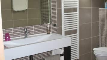 A bathroom with a white sink, mirror, and toilet. There is a towel rack with a towel hanging on it, and a bottle of soap on the sink.