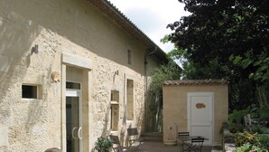Un edificio rústico de piedra con un pequeño jardín, mesas al aire libre y una puerta con una placa decorativa.