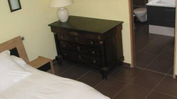 A bedroom with a bed, a dresser, a nightstand, a framed picture, and an open door to a bathroom.