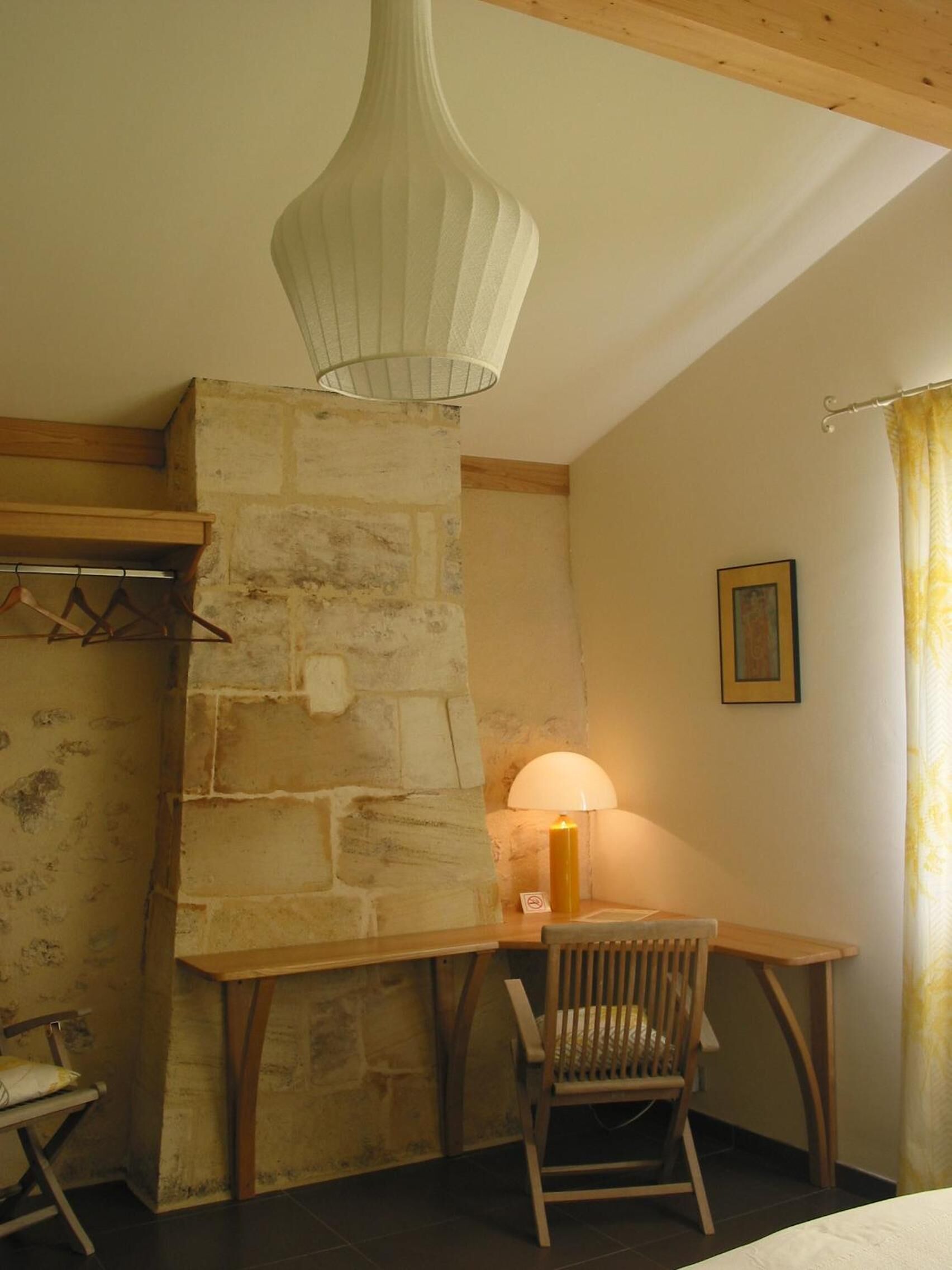 Una habitación con chimenea de piedra, un escritorio de madera, una silla y una lámpara colgante.