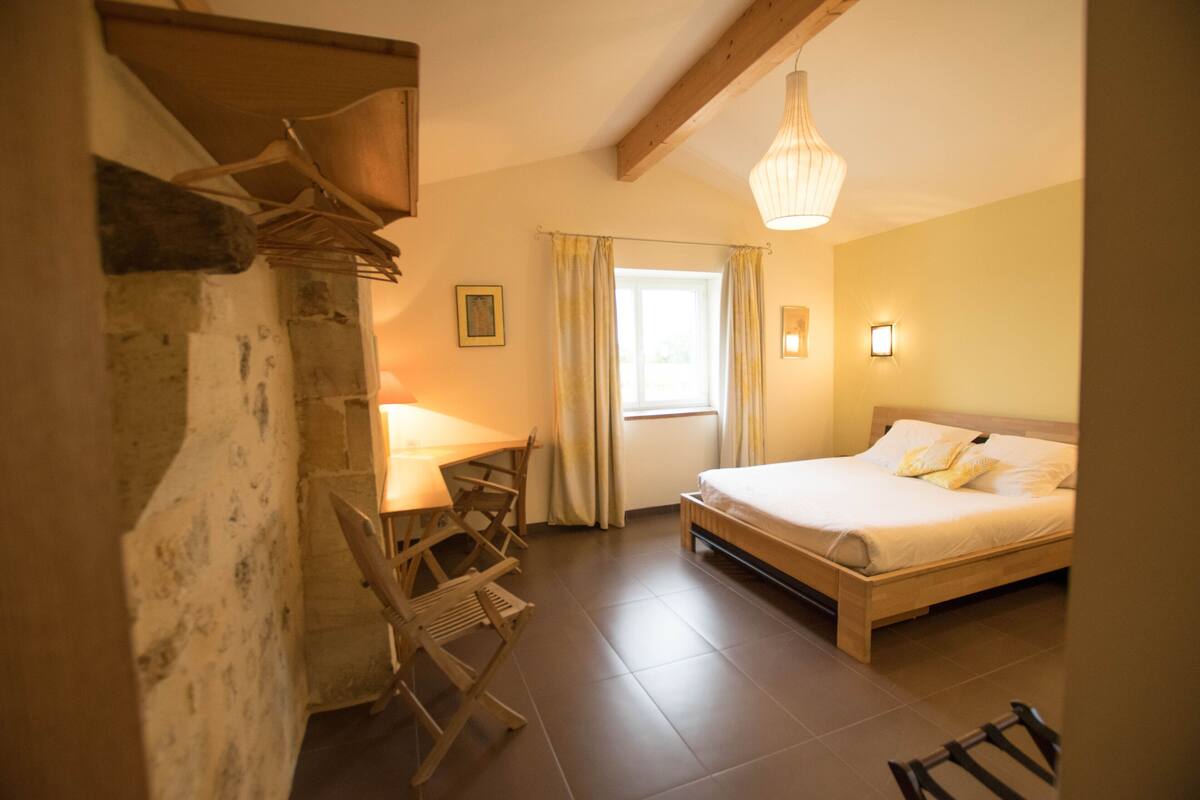 Un dormitorio con cama de madera, un escritorio con silla, una ventana con cortinas y una lámpara colgante.