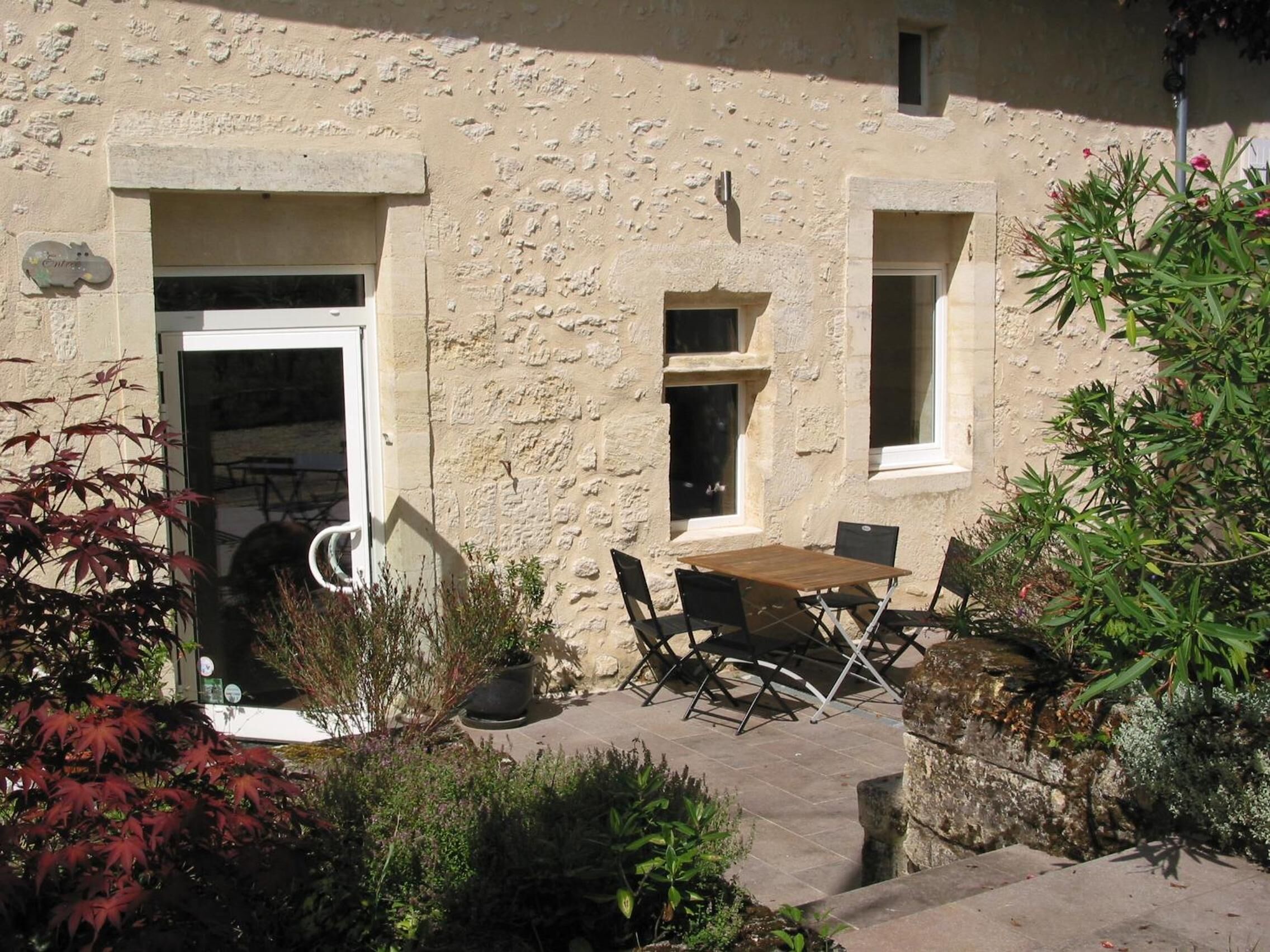 A stone building with a door, windows, and a patio area with a table and chairs.