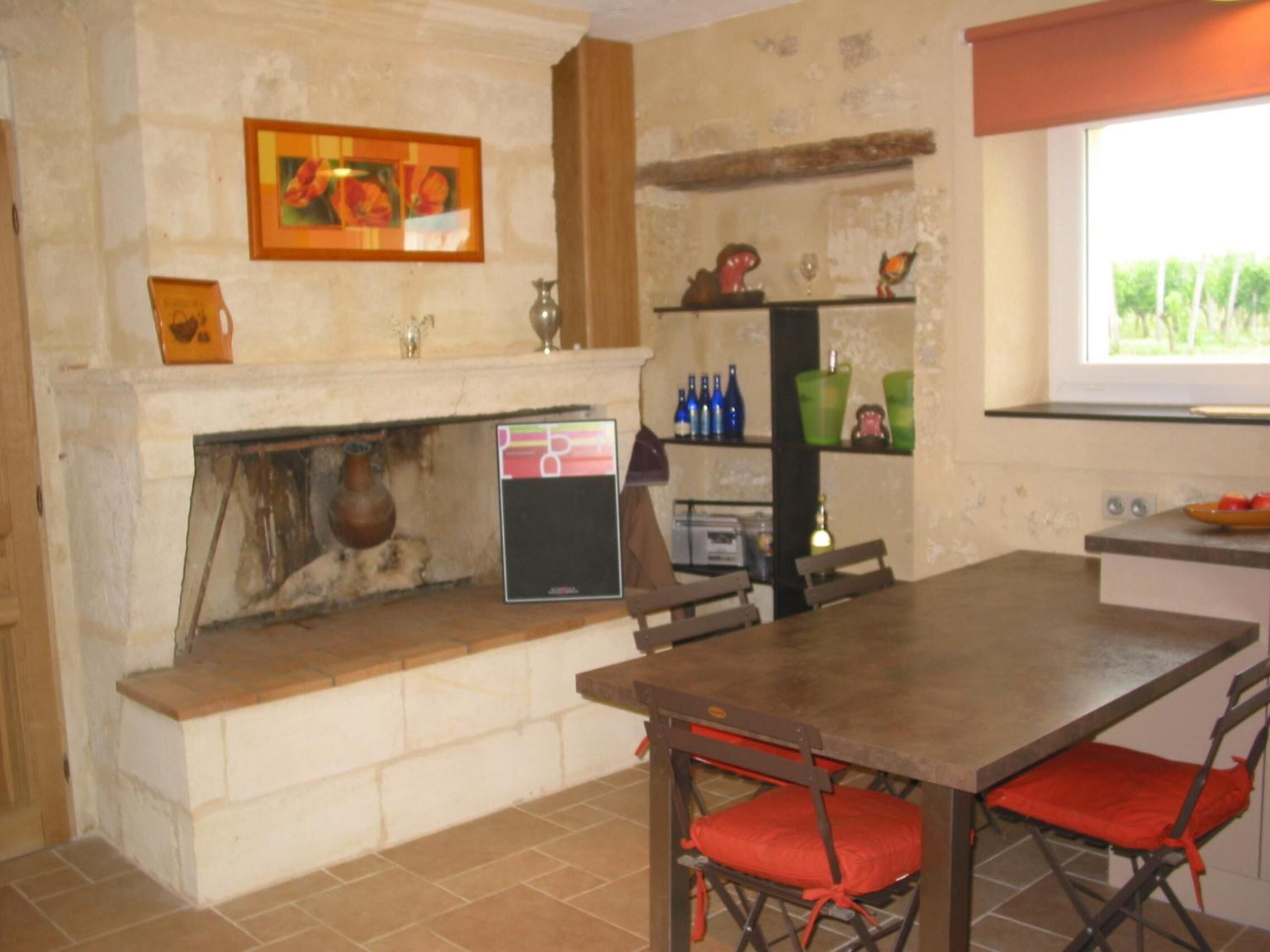 A kitchen with a stone wall, a fireplace, a shelf with bottles, and a window.