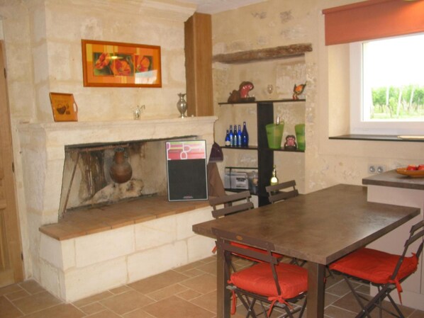 A kitchen with a stone wall, a fireplace, a shelf with bottles, and a window. - Les Secrets de Tifayne (Puisseguin)
