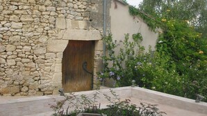 Un edificio de piedra con puerta de madera, un pequeño jardín con flores y un árbol con flores amarillas.