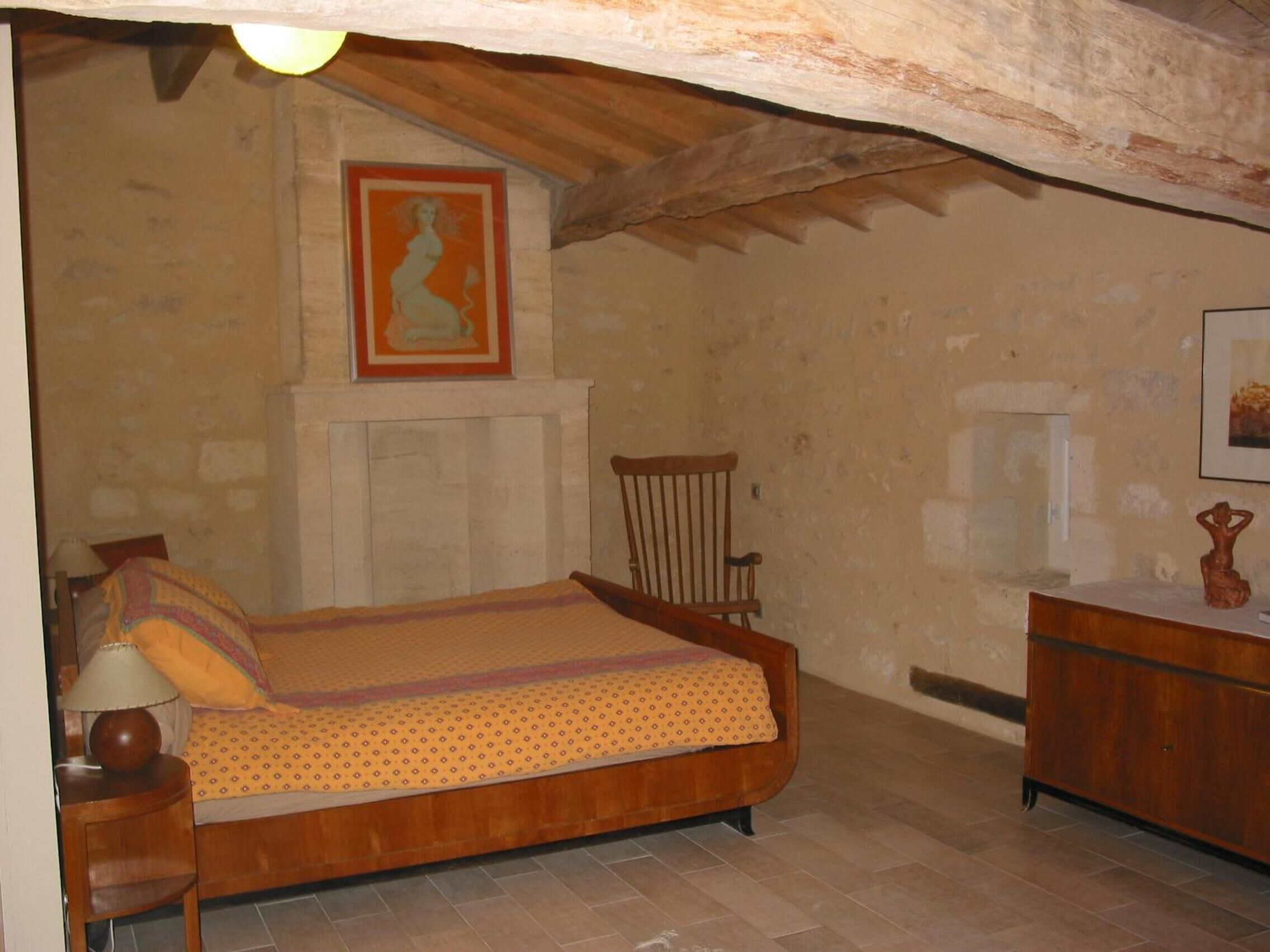 Un dormitorio con cama de madera, una silla, un tocador y un cuadro en la pared.