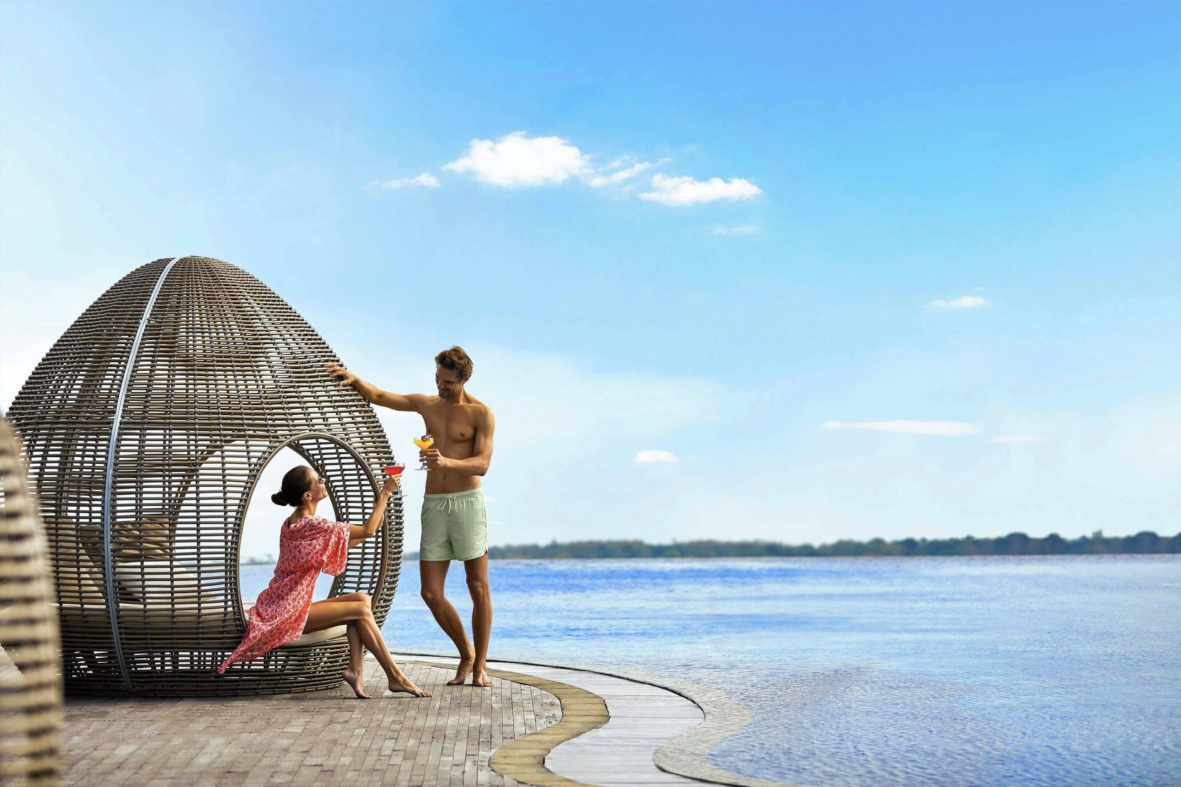 Una pareja junto a la playa, cerca de una estructura de mimbre y con una vista despejada del mar.