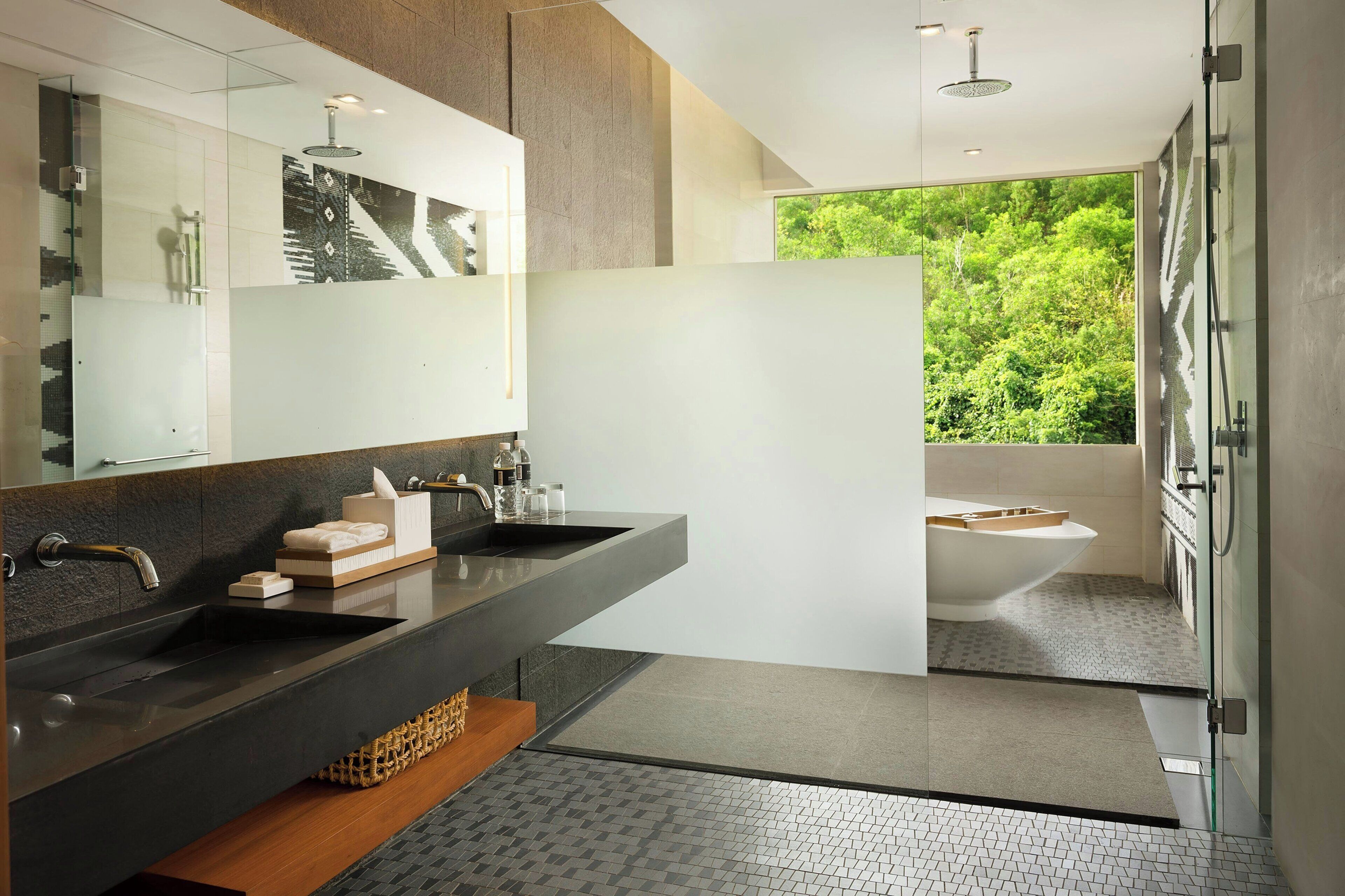 Ein modernes Badezimmer mit einem großen Spiegel, zwei Waschbecken, einer Badewanne und Blick ins Grüne.