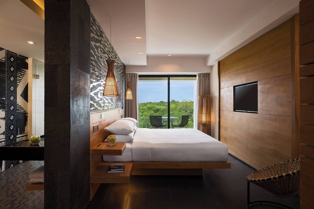 A modern hotel room with a large bed, a TV, and a view of the outdoors.