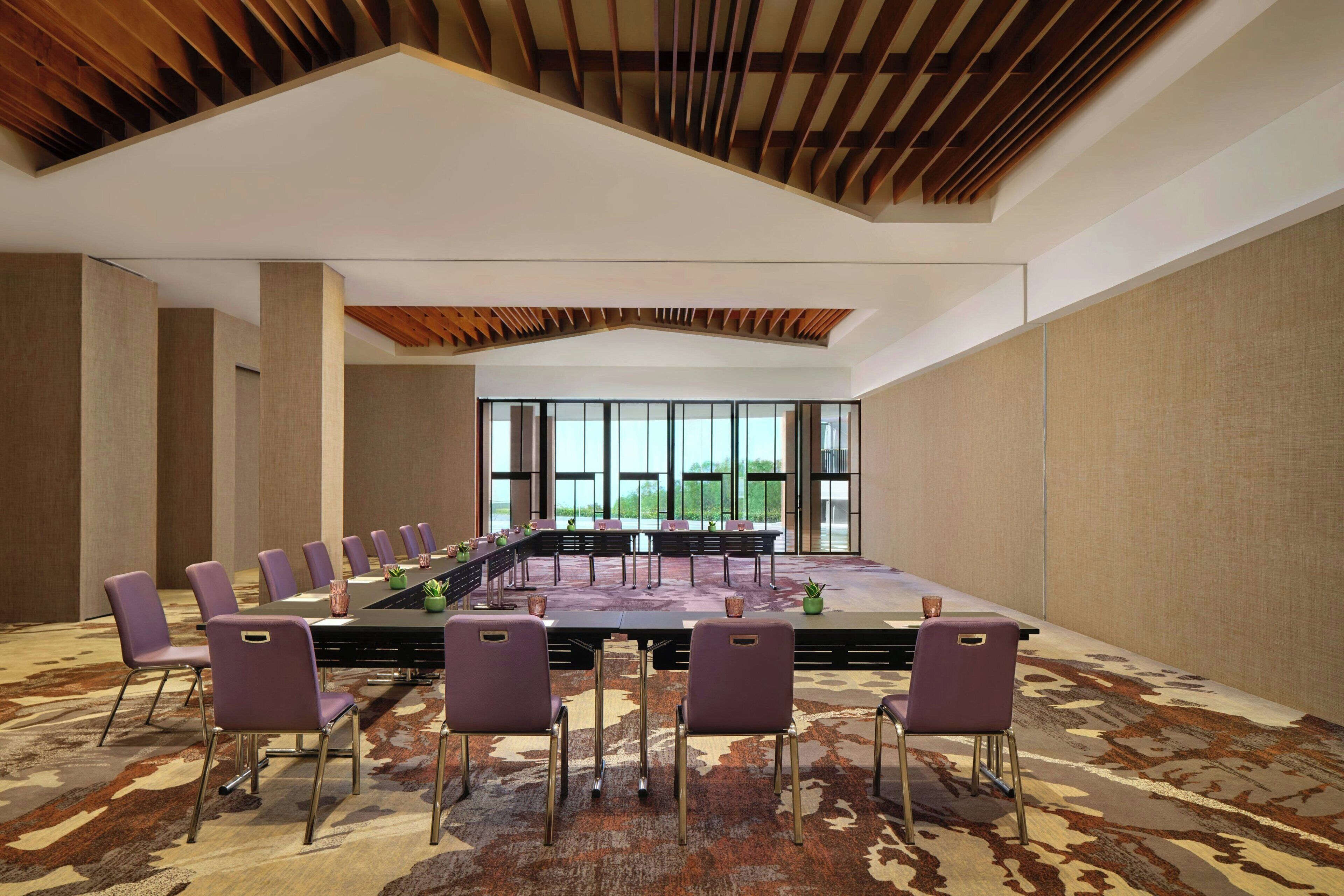 A conference room with a long table, purple chairs, and a patterned carpet.